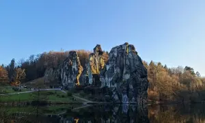 Felsformationen am Seeufer mit Spiegelung im Wasser und bewaldetem Hintergrund.