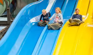 Drei Kinder rutschen lachend auf bunten Wasserrutschen.