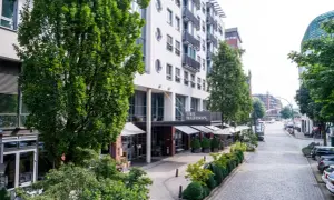 Das Madison Hotel Hamburg mit seinem Eingangsbereich und Außenbereich, umgeben von Bäumen und einer Kopfsteinpflasterstraße.