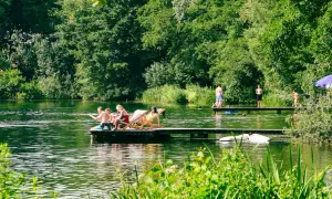 Menschen entspannen und schwimmen an einem sonnigen Tag an einem See mit üppiger Vegetation.