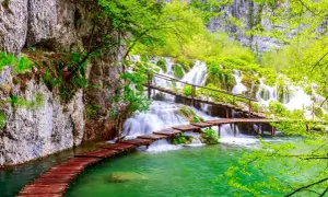 Holzstege über türkisfarbenes Wasser führen zu mehreren Wasserfällen im Grünen.