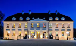 Beleuchtetes Schloss mit vielen Fenstern bei Nacht vor blauem Himmel.