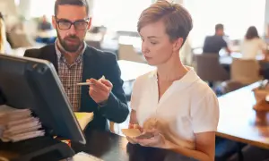 Mann mit Brille und Frau besprechen etwas am Kassensystem in einem Restaurant.