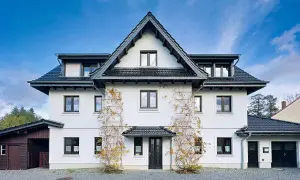 Weißes Haus mit dunklem Dach und Klinker-Vorplatz, bewachsen mit Weinreben.