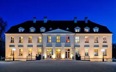 Beleuchtetes Schloss mit vielen Fenstern bei Nacht vor blauem Himmel.