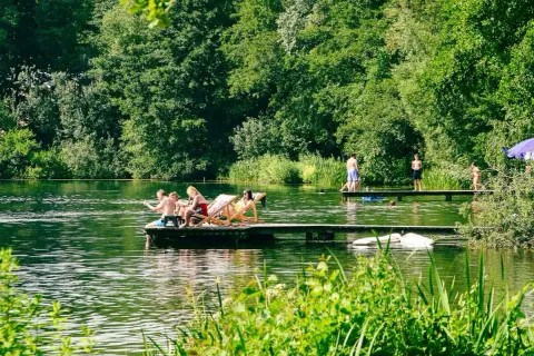 Menschen entspannen und schwimmen an einem sonnigen Tag an einem See mit üppiger Vegetation.