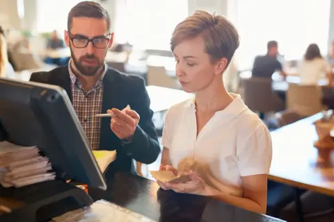 Mann mit Brille und Frau besprechen etwas am Kassensystem in einem Restaurant.
