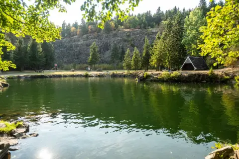 Grüner See mit Bäumen, Felsen und einem kleinen Unterstand am Ufer.