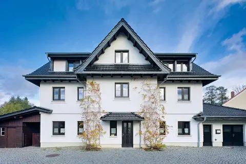 Weißes Haus mit dunklem Dach und Klinker-Vorplatz, bewachsen mit Weinreben.