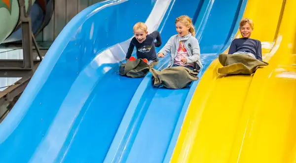 Drei Kinder rutschen lachend auf bunten Wasserrutschen.