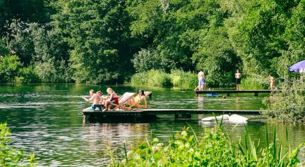 Menschen entspannen und schwimmen an einem sonnigen Tag an einem See mit üppiger Vegetation.