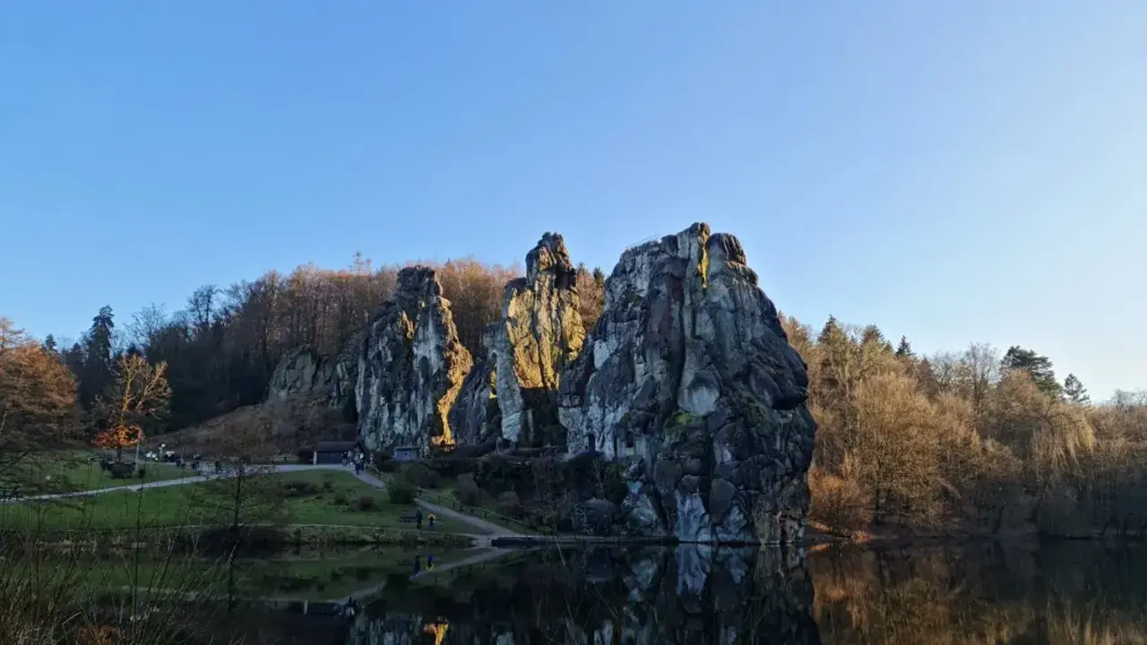 Felsformationen am Seeufer mit Spiegelung im Wasser und bewaldetem Hintergrund.