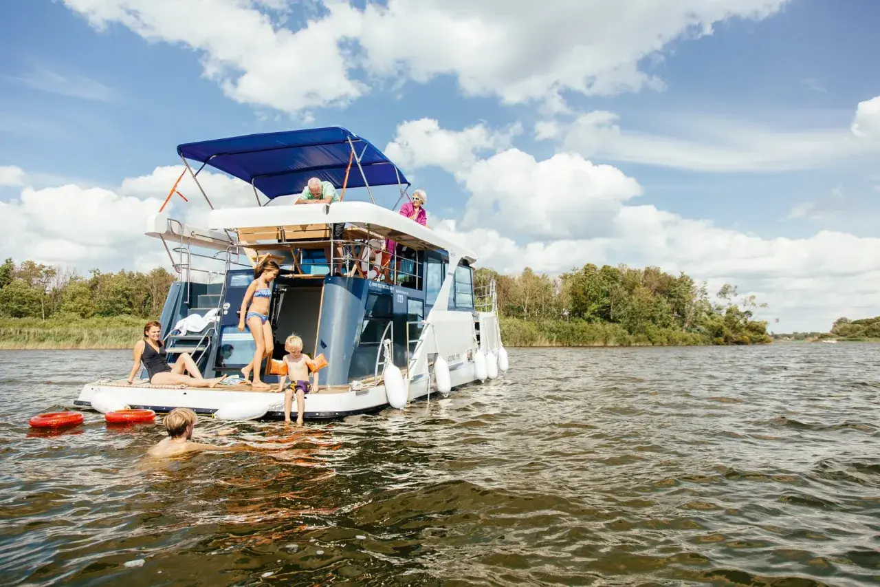Familie auf einem Hausboot in der Mecklenburgischen Seenplatte, einige schwimmen, andere entspannen sich.